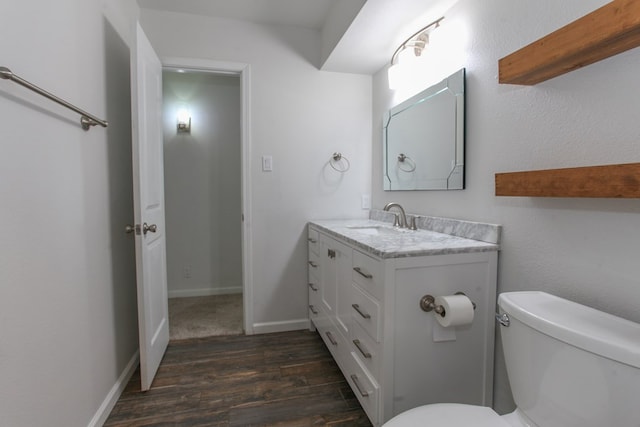 half bathroom with vanity, toilet, wood finished floors, and baseboards