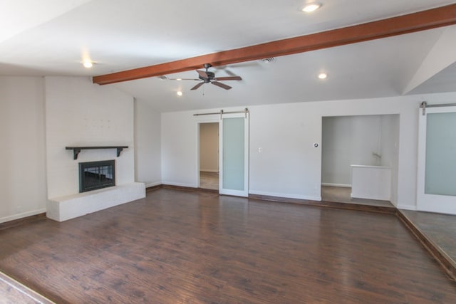 unfurnished living room with a glass covered fireplace, a barn door, vaulted ceiling with beams, and wood finished floors