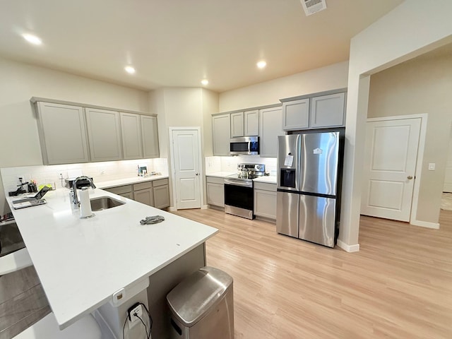 kitchen with gray cabinets, appliances with stainless steel finishes, tasteful backsplash, a breakfast bar area, and kitchen peninsula