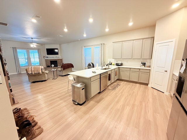 kitchen featuring sink, tasteful backsplash, a brick fireplace, stainless steel dishwasher, and kitchen peninsula