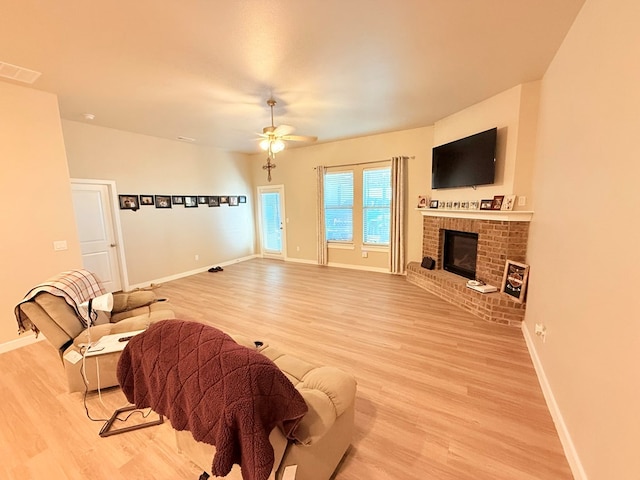 living room featuring a brick fireplace, light hardwood / wood-style floors, and ceiling fan