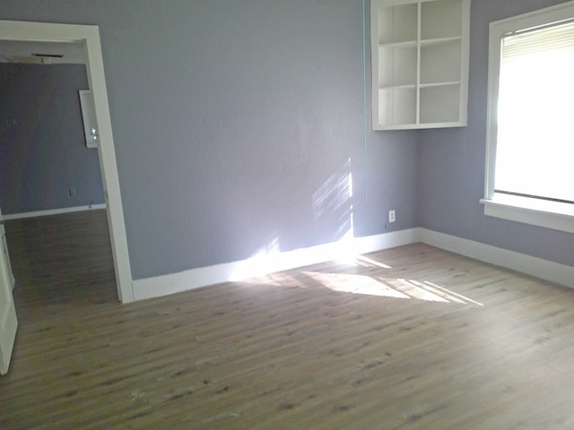 empty room featuring wood-type flooring, plenty of natural light, and built in features