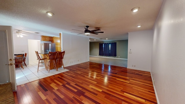 living area with ceiling fan, a textured ceiling, baseboards, and light wood-style floors