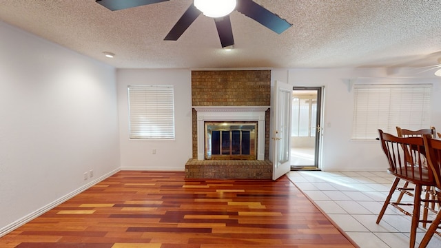 living room with a brick fireplace, a textured ceiling, a ceiling fan, and wood finished floors