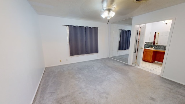 unfurnished bedroom featuring light colored carpet, light tile patterned flooring, a textured ceiling, ensuite bath, and baseboards