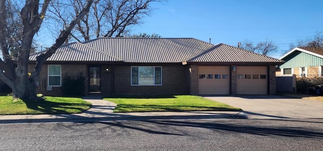 ranch-style house featuring an attached garage, metal roof, concrete driveway, and a front yard