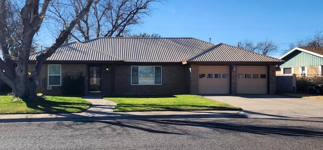 ranch-style home with a garage, metal roof, a front lawn, and driveway