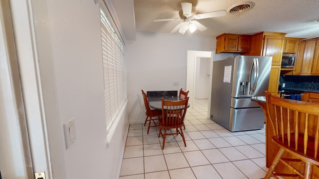 kitchen with visible vents, brown cabinetry, dark countertops, appliances with stainless steel finishes, and light tile patterned flooring