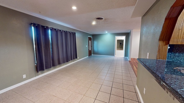 empty room featuring visible vents, ornamental molding, light tile patterned flooring, a textured ceiling, and baseboards