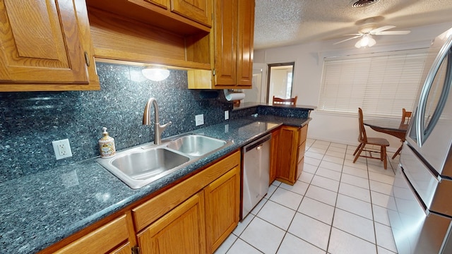 kitchen with light tile patterned floors, brown cabinetry, appliances with stainless steel finishes, a textured ceiling, and a sink