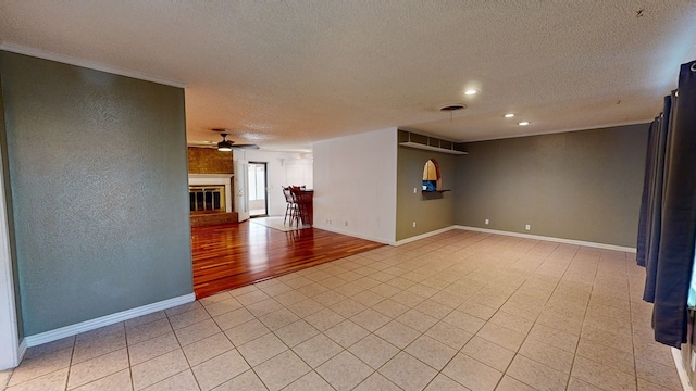 unfurnished room featuring a glass covered fireplace, ceiling fan, a textured ceiling, and baseboards