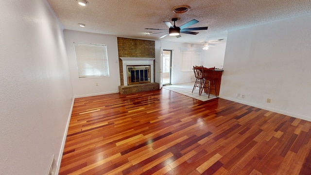 unfurnished living room with visible vents, a brick fireplace, ceiling fan, a textured ceiling, and wood finished floors