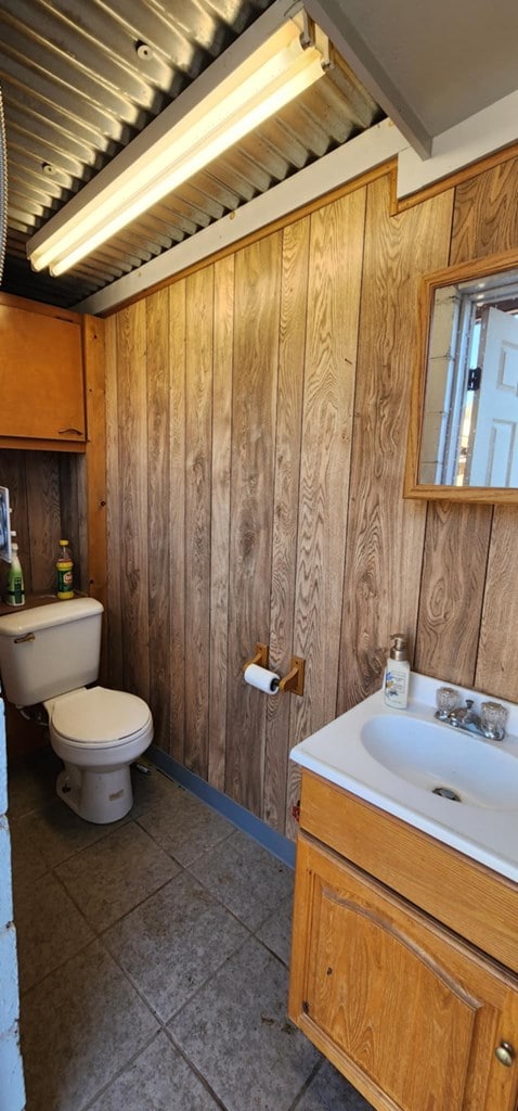 bathroom featuring toilet, wood walls, tile patterned flooring, and vanity