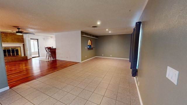 unfurnished room with a brick fireplace, ceiling fan, baseboards, and a textured ceiling