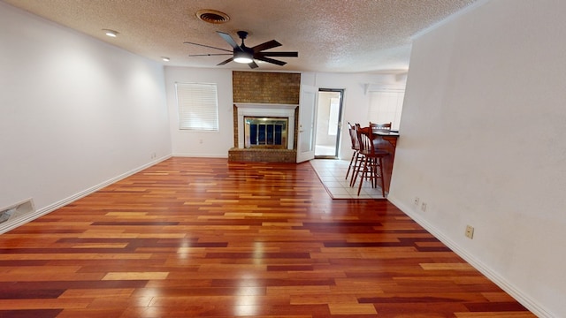 unfurnished living room with a large fireplace, visible vents, a ceiling fan, dark wood-style floors, and a textured ceiling