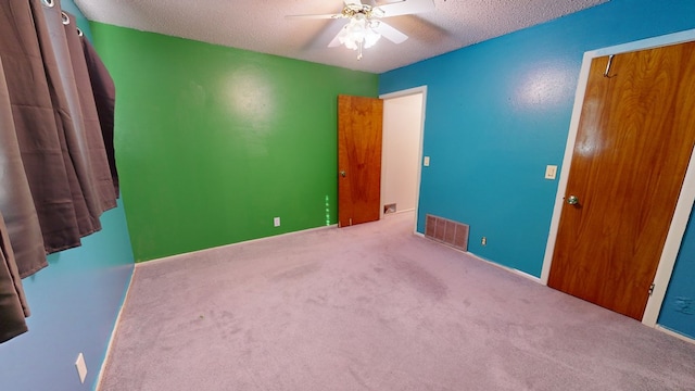 unfurnished bedroom with a textured ceiling, ceiling fan, carpet flooring, and visible vents