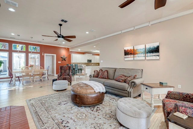 living room featuring ceiling fan, ornamental molding, light wood finished floors, and visible vents
