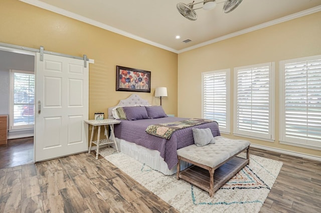 bedroom with visible vents, ornamental molding, a barn door, and wood finished floors