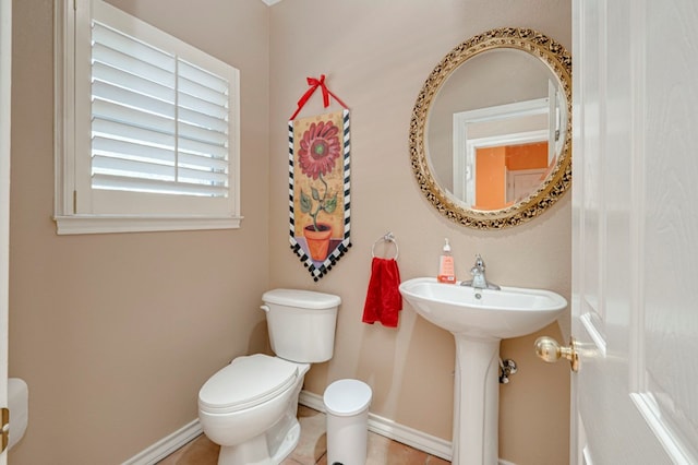 half bath featuring baseboards, a sink, tile patterned floors, and toilet