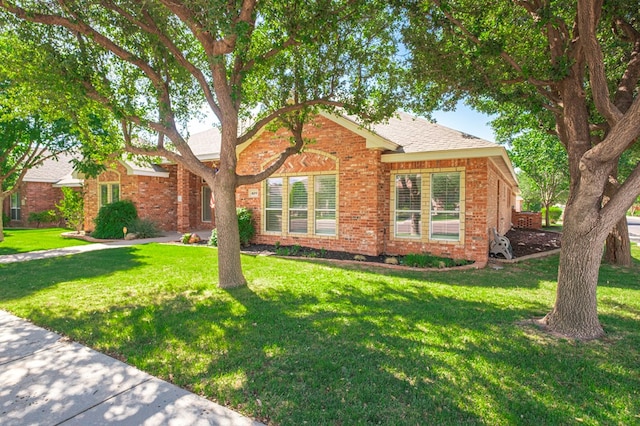 ranch-style home featuring roof with shingles, a front yard, and brick siding