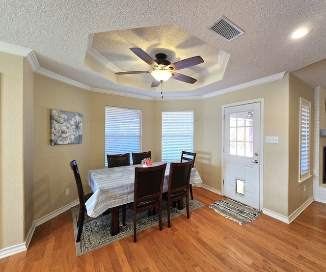 dining space with a raised ceiling, wood-type flooring, a textured ceiling, and crown molding