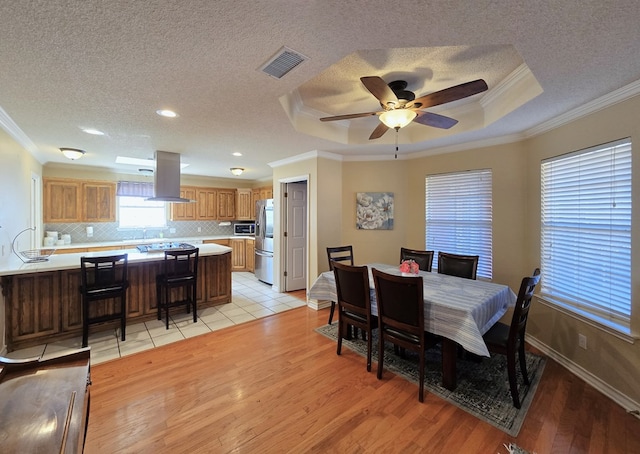 dining area featuring crown molding, a raised ceiling, light hardwood / wood-style flooring, and a textured ceiling