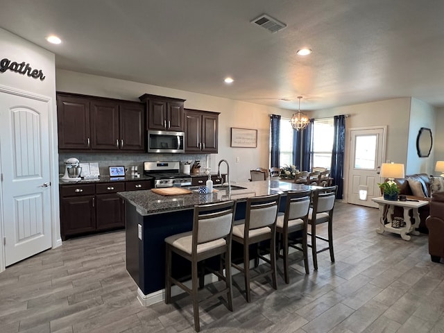 8409 E County Rd 113, Midland, TX 79706 - kitchen with stainless steel appliances, a kitchen bar, a chandelier, light wood-style floors, and dark stone counters