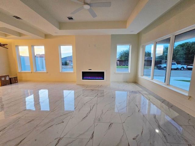 2607 Hoya Dr, Midland, TX 79707 - unfurnished living room with ceiling fan, a tray ceiling, a lit fireplace, and healthy amount of natural light