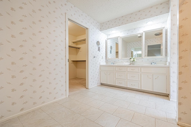 1007 Shirley Ln, Midland, TX 79705 - bathroom with wallpapered walls, double vanity, tile patterned flooring, a textured ceiling, and a walk in closet