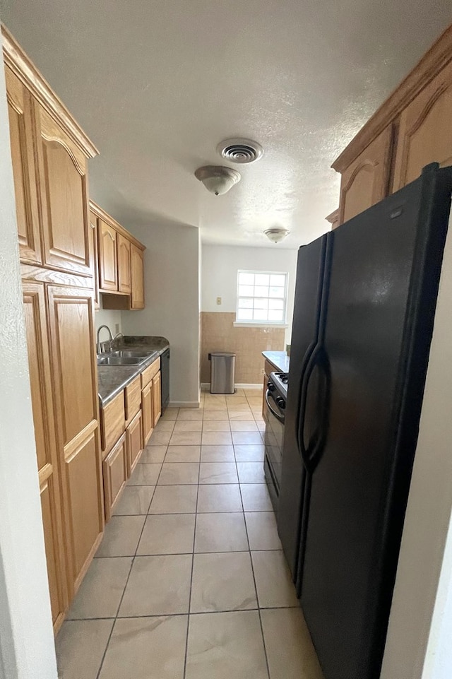 kitchen featuring a textured ceiling, light tile patterned flooring, a sink, visible vents, and black appliances