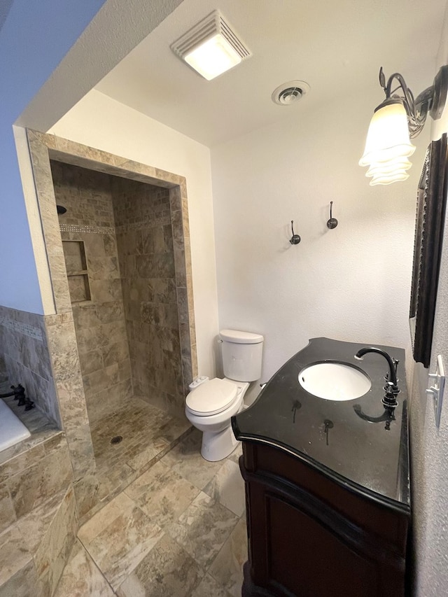 bathroom with toilet, visible vents, a tile shower, and vanity