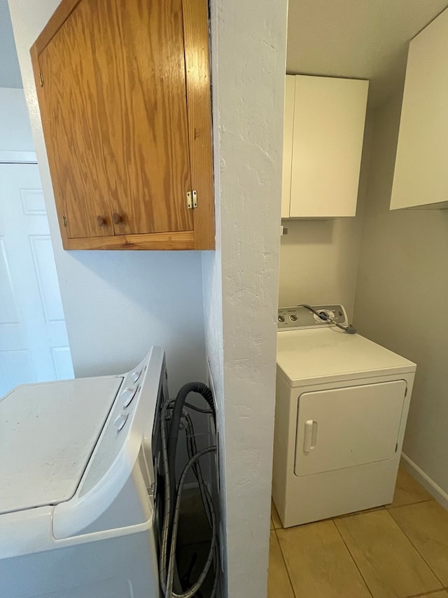 laundry area featuring light tile patterned floors, cabinet space, and baseboards