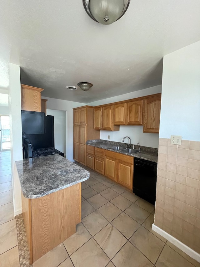 kitchen with light tile patterned flooring, a sink, dark stone countertops, dishwasher, and a peninsula