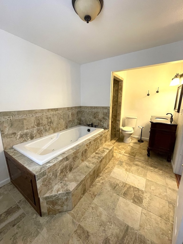 bathroom with a jetted tub, vanity, toilet, and baseboards