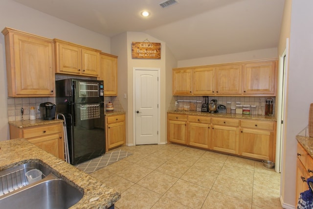 kitchen featuring lofted ceiling, backsplash, black fridge, light tile patterned floors, and light stone counters