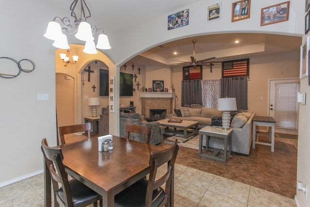 tiled dining room featuring ceiling fan with notable chandelier and a raised ceiling