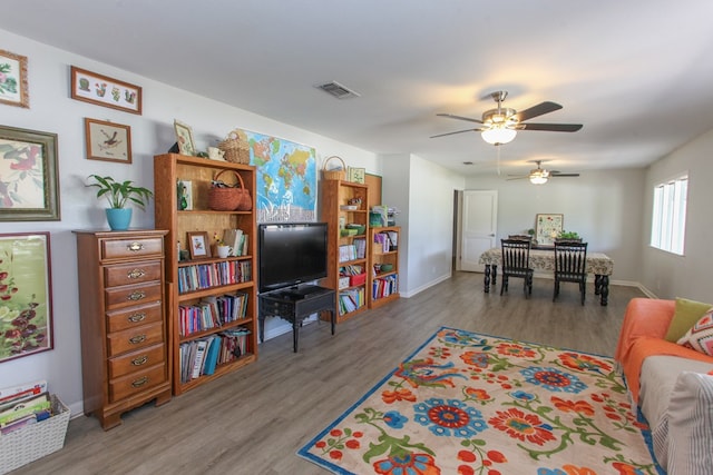 living area with baseboards, ceiling fan, wood finished floors, and visible vents