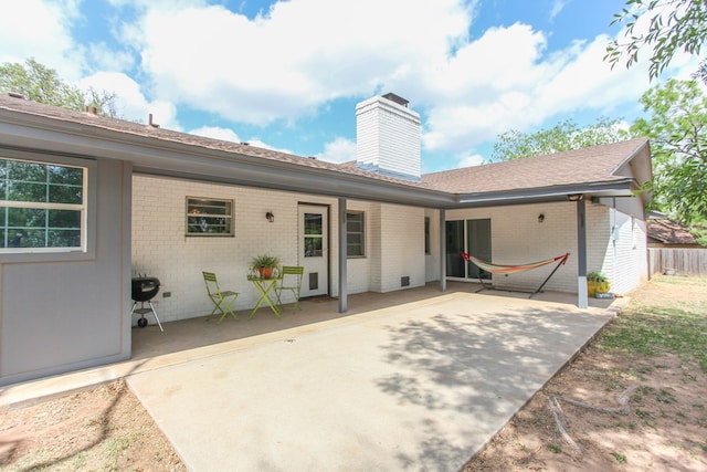 rear view of property featuring a chimney, brick siding, fence, a patio, and a shingled roof