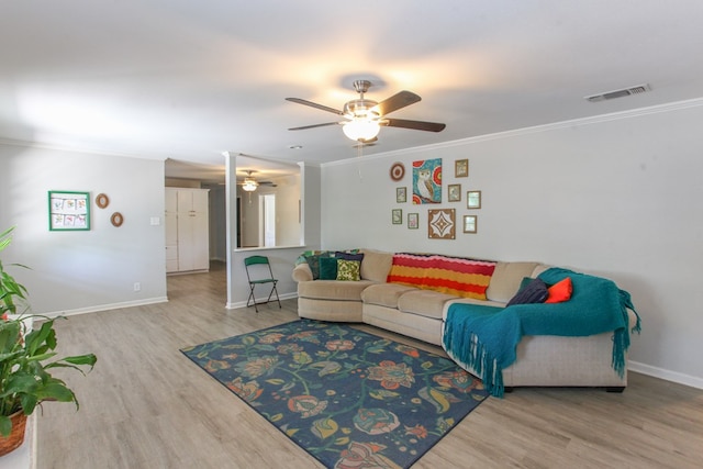 living room with a ceiling fan, baseboards, wood finished floors, visible vents, and ornamental molding