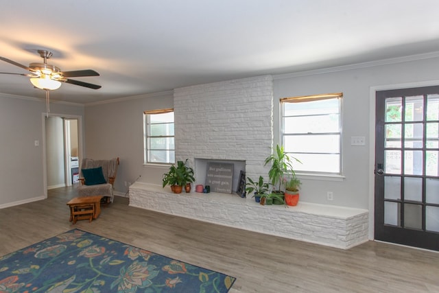 living area with a ceiling fan, crown molding, a brick fireplace, wood finished floors, and baseboards
