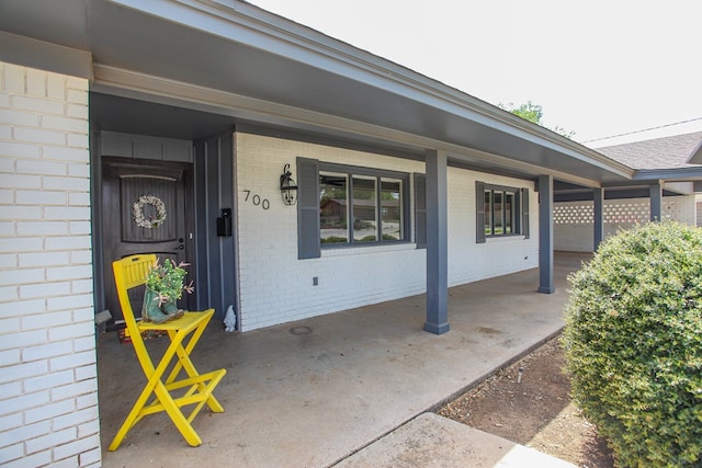 doorway to property featuring covered porch and brick siding