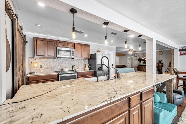 kitchen with hanging light fixtures, light stone counters, crown molding, and stainless steel appliances