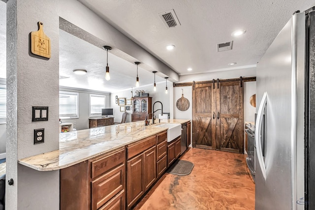 kitchen with a textured ceiling, appliances with stainless steel finishes, sink, hanging light fixtures, and a barn door