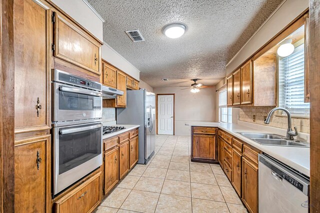2821 Metz Dr, Midland, TX 79705 - kitchen featuring stainless steel appliances, a sink, a ceiling fan, brown cabinets, and a textured ceiling