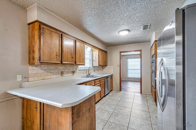 2821 Metz Dr, Midland, TX 79705 - kitchen featuring appliances with stainless steel finishes, brown cabinetry, a sink, a peninsula, and decorative backsplash