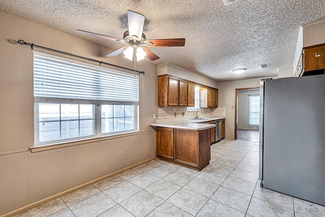 2821 Metz Dr, Midland, TX 79705 - kitchen with stainless steel appliances, brown cabinetry, a peninsula, light countertops, and plenty of natural light
