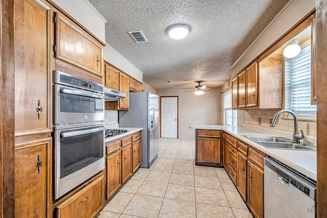2821 Metz Dr, Midland, TX 79705 - kitchen featuring stainless steel appliances, a sink, a ceiling fan, brown cabinets, and a textured ceiling