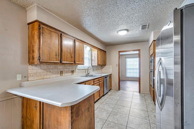 2821 Metz Dr, Midland, TX 79705 - kitchen featuring appliances with stainless steel finishes, brown cabinetry, a sink, a peninsula, and decorative backsplash
