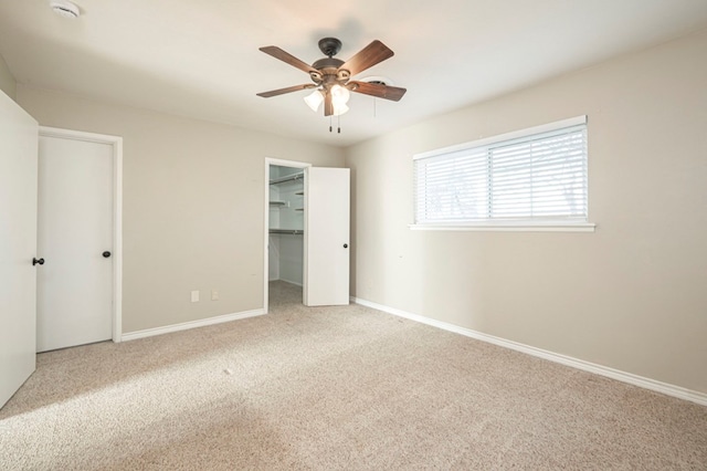 unfurnished bedroom with a ceiling fan, carpet, a walk in closet, and baseboards