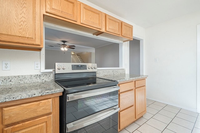 kitchen with light brown cabinetry, range with two ovens, a ceiling fan, and baseboards